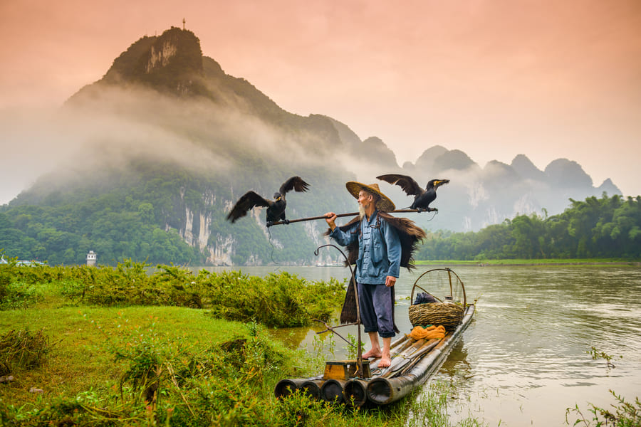 Hombre pescando con dos pájaros a lado en Yangshuo